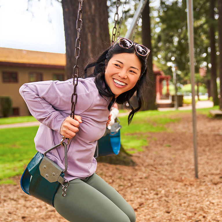 Una mujer sonriente balanceándose en un columpio en un parque de juegos.