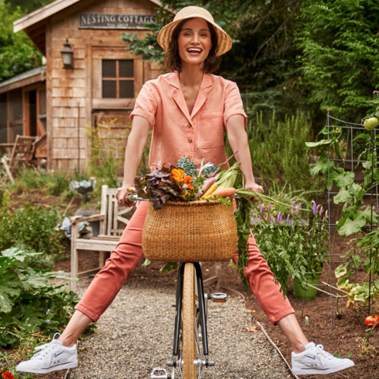 Mujer en bicicleta en un huerto. La cesta de la bicicleta está llena de verduras frescas.